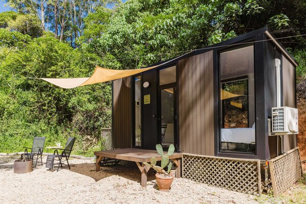 A small wooden cabin with a patio, a table, chairs, and a cactus plant.