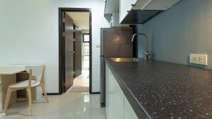 A modern kitchen with a dark countertop, a stainless steel refrigerator, and a wooden chair. - 100mBeachfront gym Swimming Pools c100 (Rawai)
