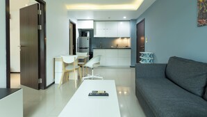 A modern living room with a grey sofa, a white coffee table, and a dining area with a white table and chairs. - 100mBeachfront gym Swimming Pools c100 (Rawai)