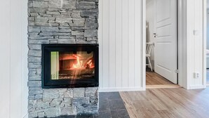 Une cheminée en pierre avec un feu apparent, des lambris blancs sur le mur et un plancher en bois.