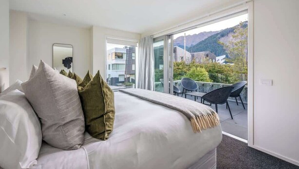 Habitación de hotel moderna con una cama grande, un balcón con sillas y vistas del entorno.