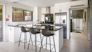Una cocina moderna con una isla central, taburetes de bar, electrodomésticos de acero inoxidable y un amplio ventanal.
