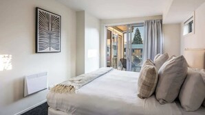 Habitación de hotel con cama, almohadas, radiador, una obra de arte enmarcada y vistas a través de un ventanal.