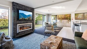 Una sala de estar moderna con chimenea, un televisor montado en una pared de piedra y un comedor con vistas al exterior.