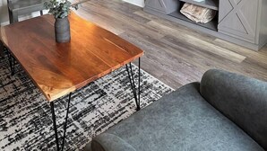 Un soggiorno con un tavolino in legno, un divano grigio, una TV su un mobile TV grigio, una sveglia al muro e una scala sullo sfondo.