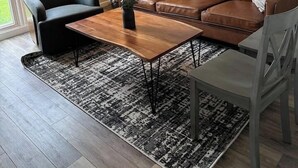 Un soggiorno moderno con un divano in pelle marrone, una poltrona nera, un tavolino in legno e un tappeto decorato.