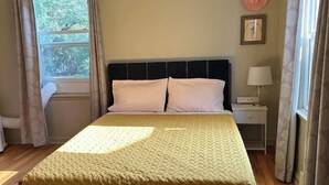 A bedroom with a bed, a nightstand, a window with curtains, and a wall-mounted hat.