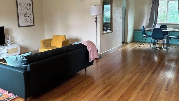 A spacious living area with a black sofa, a yellow chair, and a dining table with chairs.