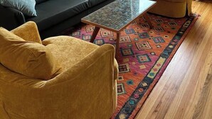 A living room with a black sofa, a yellow armchair, a glass coffee table, and a colorful rug.