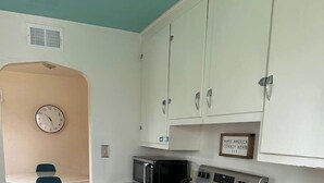 A compact kitchen with white cabinets, a microwave, an oven, and a small dining area with a chair and table.
