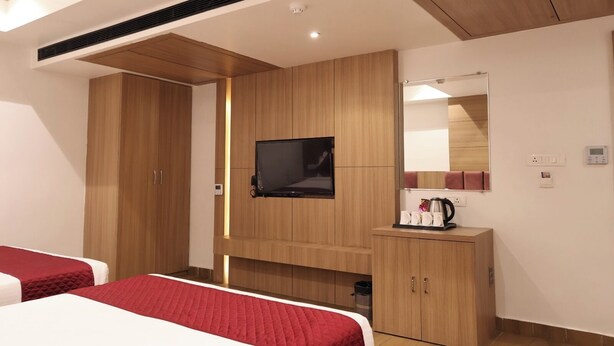 A hotel room with two beds, a TV mounted on the wall, a mirror, and a small table with a kettle and cups. - Hotel Priydarshan (Kanpur)