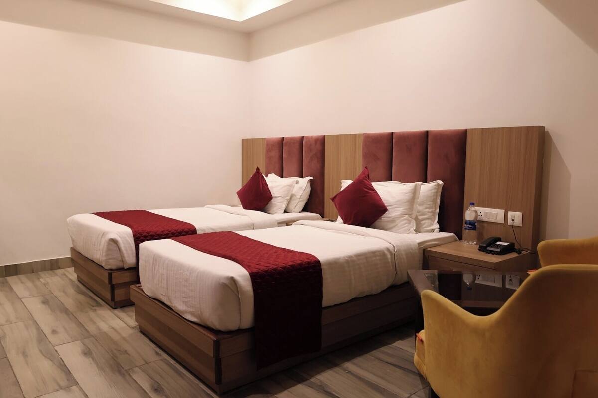 A hotel room with two beds, a wooden headboard, a bedside table with a phone and water bottle, and a yellow chair.