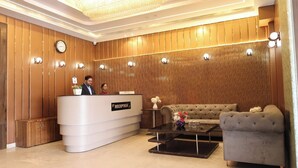 A reception area with a reception desk, a sofa, a coffee table, and a chandelier. - Hotel Priydarshan (Kanpur)