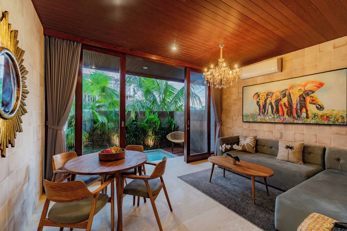 A modern living room with a wooden ceiling, a dining area with wooden chairs, a sofa, and a painting of elephants.