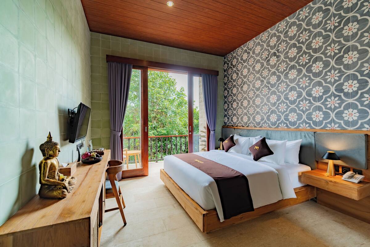 A bedroom with a bed, wooden desk, and a Buddha statue.
