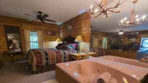 Een kamer in chaletstijl met een groot bed, een zithoek, een riant bad en een plafondventilator.