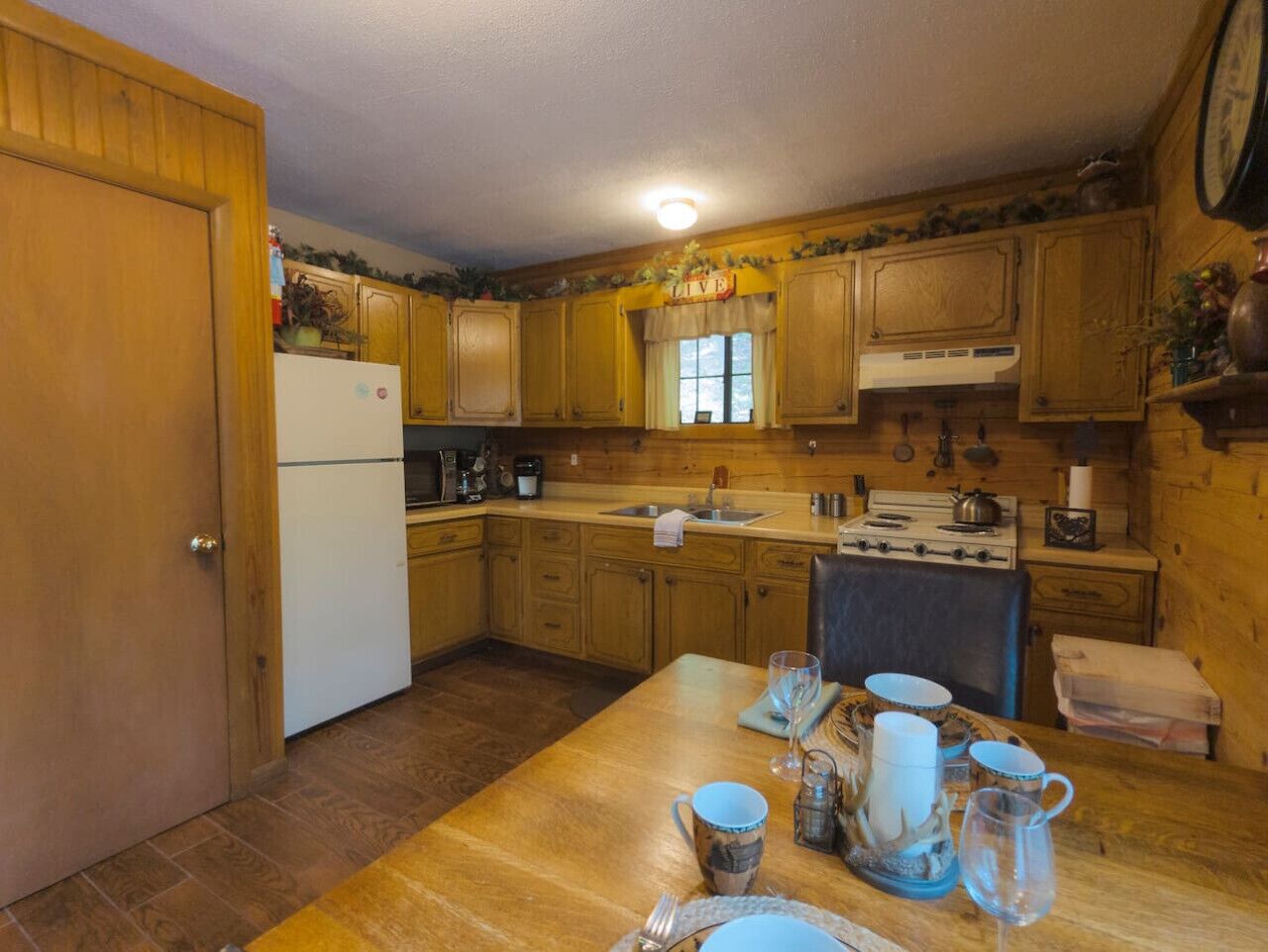 Une cuisine compacte dotée de meubles en bois, d’un réfrigérateur, d’une cuisinière et d’une table à manger, le tout agrémenté d’assiettes, de tasses et d’un verre.