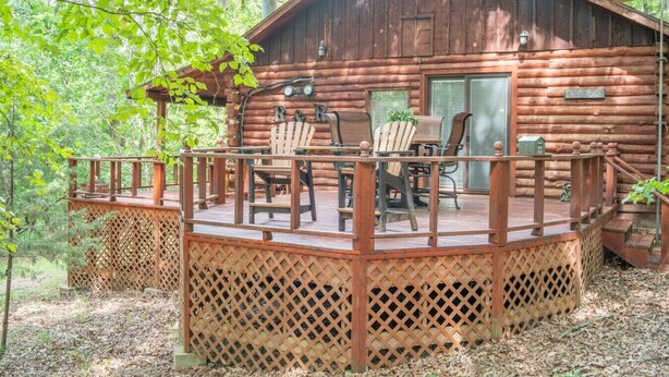 Een rustieke hut met een houten terras, voorzien van Adirondack-stoelen en een tafel.