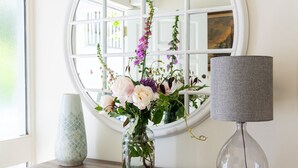 A round mirror with a white frame, a vase with flowers, a lamp, and wicker baskets on a wooden console table. - Bluefin -  a house that sleeps 6 guests  in 3 bedrooms (Salcombe)