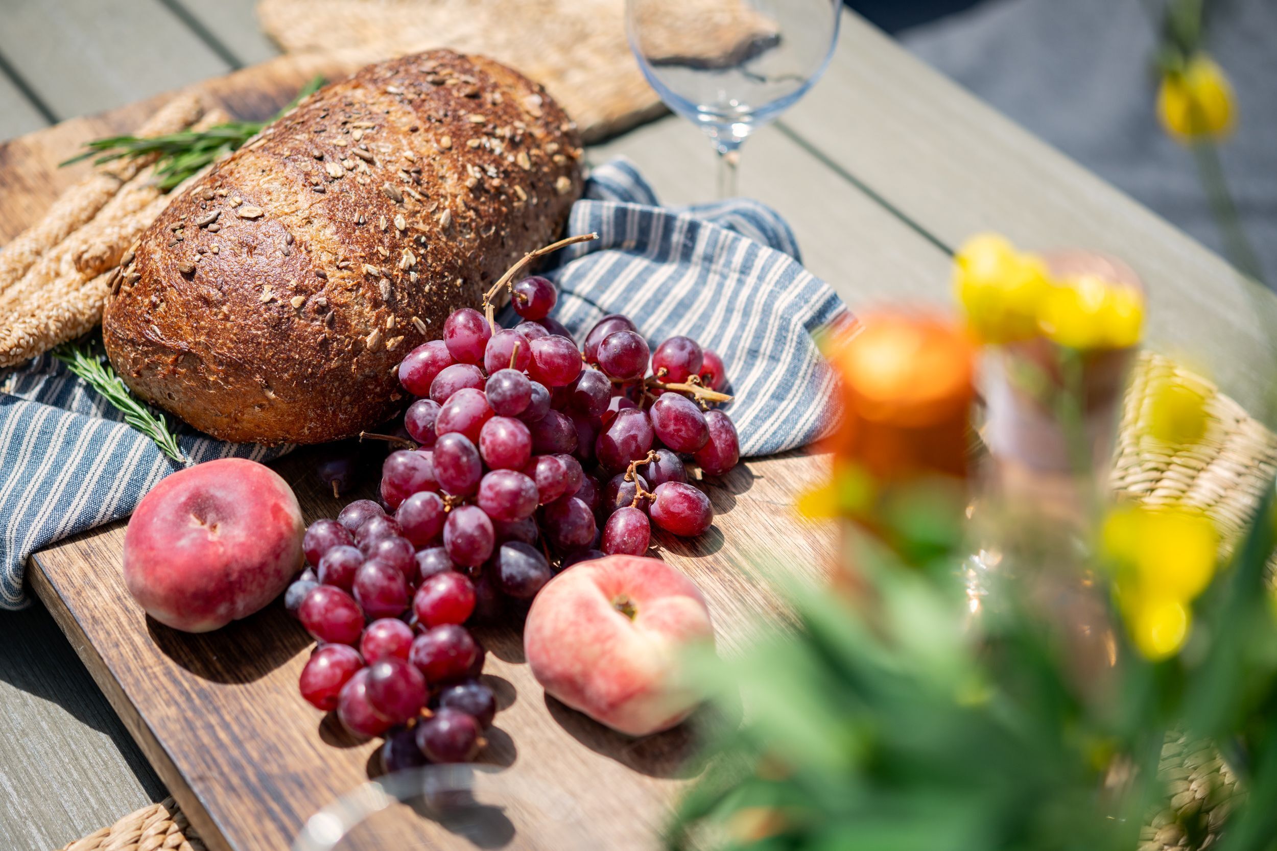 A wooden table with a loaf of bread, grapes, an apple, and a glass of wine.