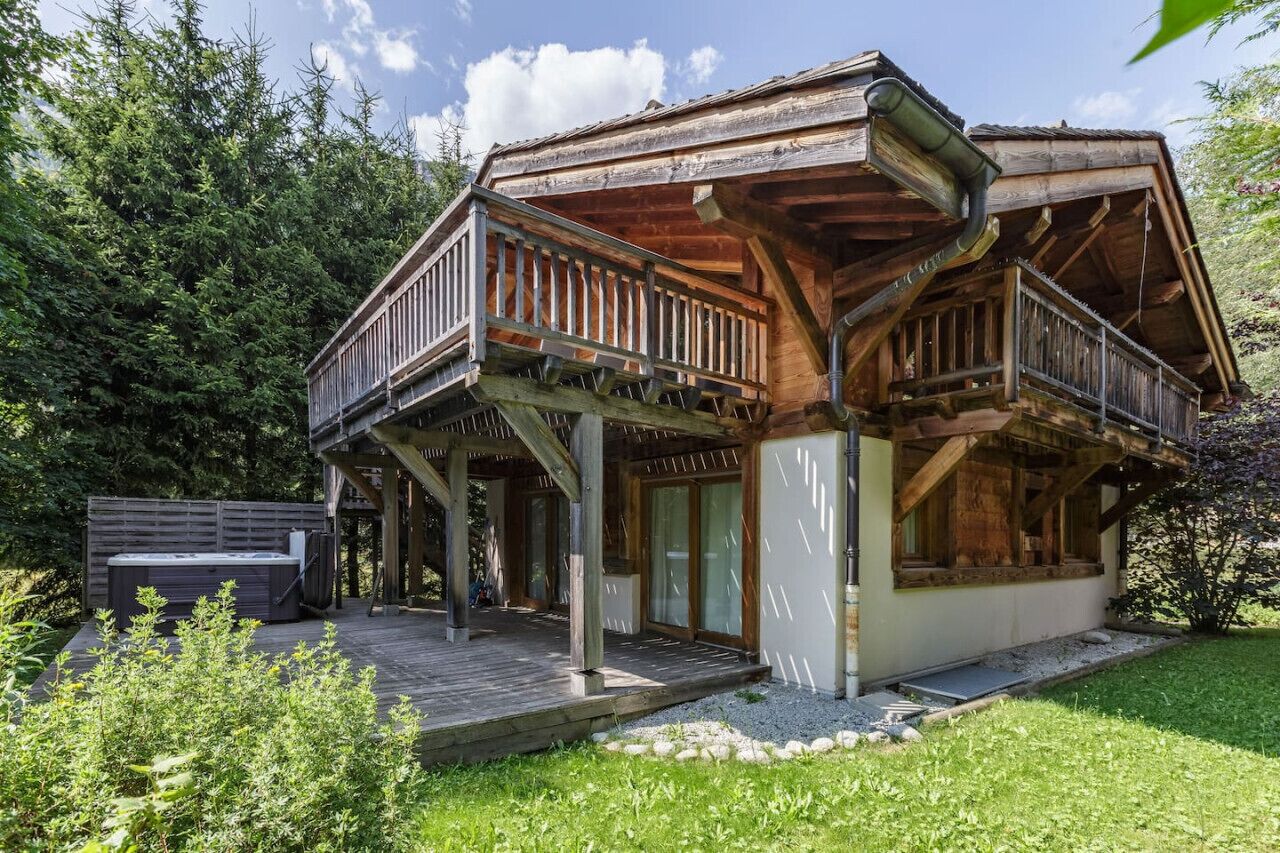 A wooden cabin with a balcony, a hot tub, and a deck.