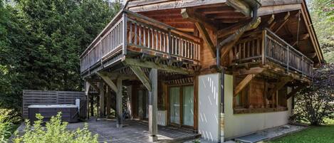 A wooden cabin with a balcony, a hot tub, and a deck.