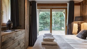 Une chambre avec un grand lit, une commode en bois, une lampe et une vue sur la verdure grâce à une porte coulissante.