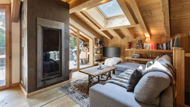 Un salon chaleureux de style loft, doté d’une cheminée, de poutres en bois, d’un grand téléviseur et d’une bibliothèque.