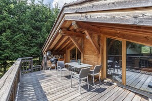 Une terrasse en bois avec une table et des chaises, entourée d’une structure en bois qui ressemble à un chalet, avec de grandes fenêtres.