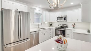 A modern kitchen with white cabinetry, stainless steel appliances, and a central island with a fruit basket. - Newly Built Home Near Morrison Rockwood State Park (Morrison)