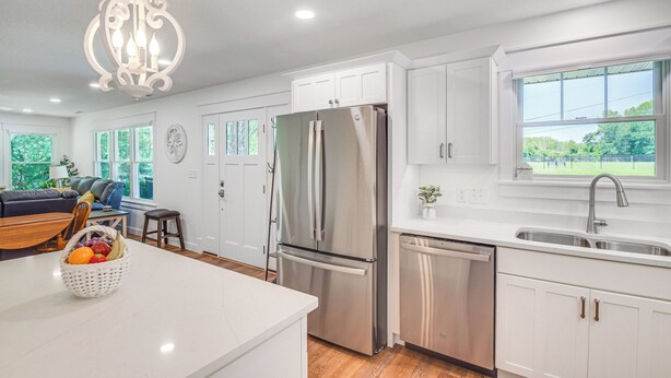 A modern kitchen with white cabinetry, stainless steel appliances, and a large window offering a view of greenery. - Newly Built Home Near Morrison Rockwood State Park (Morrison)