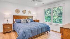 A bedroom with a large bed, wooden headboard, two bedside tables with lamps, and a large window with a view of trees. - Newly Built Home Near Morrison Rockwood State Park (Morrison)