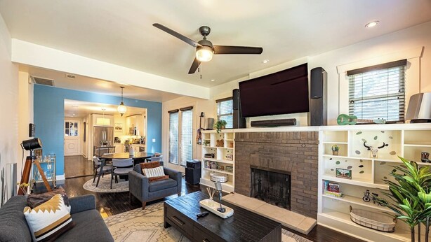 A modern living room with a fireplace, a ceiling fan, and a television.