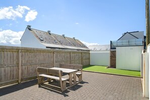 A patio with a wooden table and benches, a wooden fence, and a green lawn area. - Modern Townhouse w/ Parking nr Tolcarne Beach (Newquay)