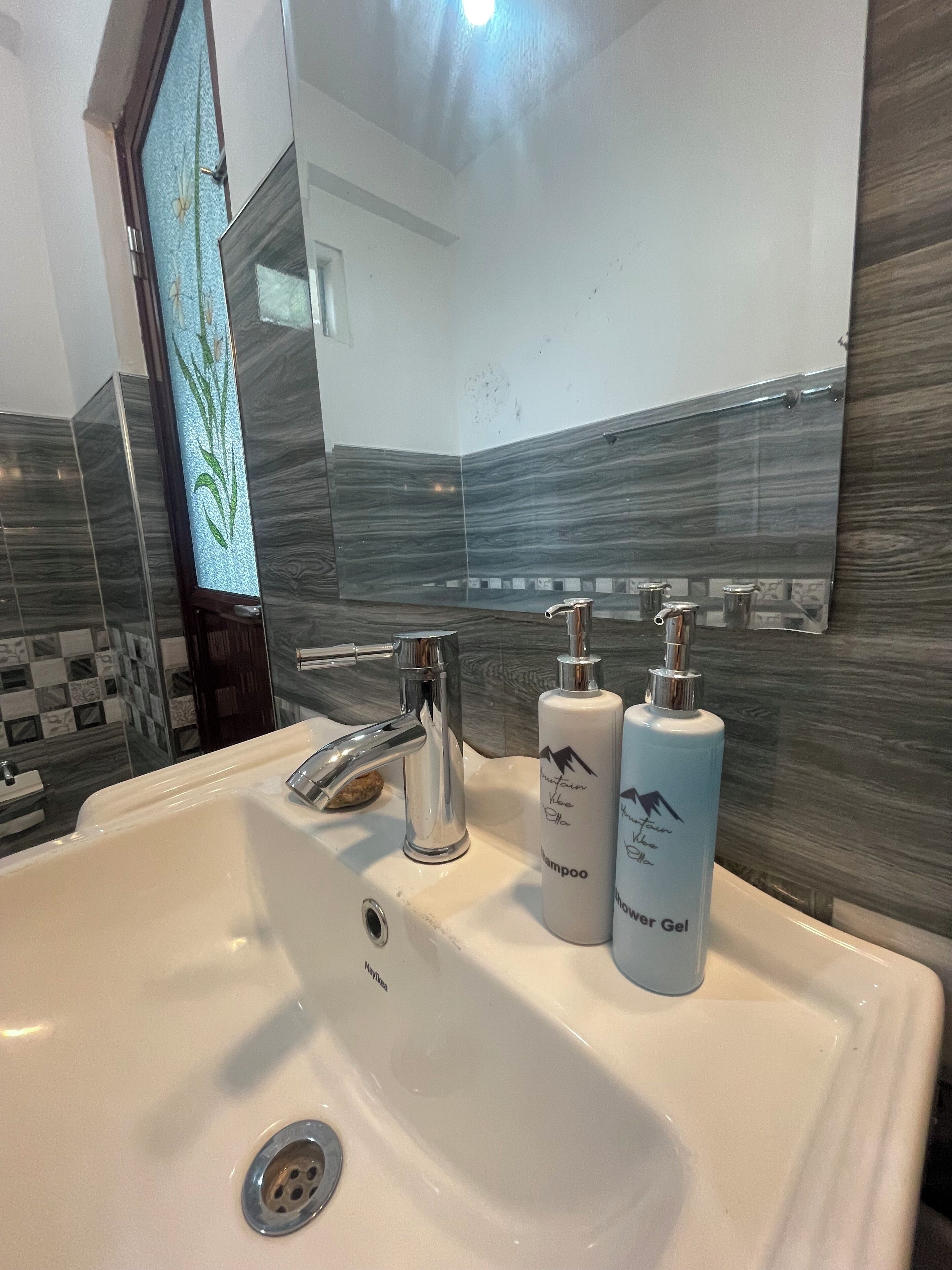 Een badkamer met een witte wastafel, twee flessen shampoo en douchegel, en een spiegel met een decoratieve lijst.