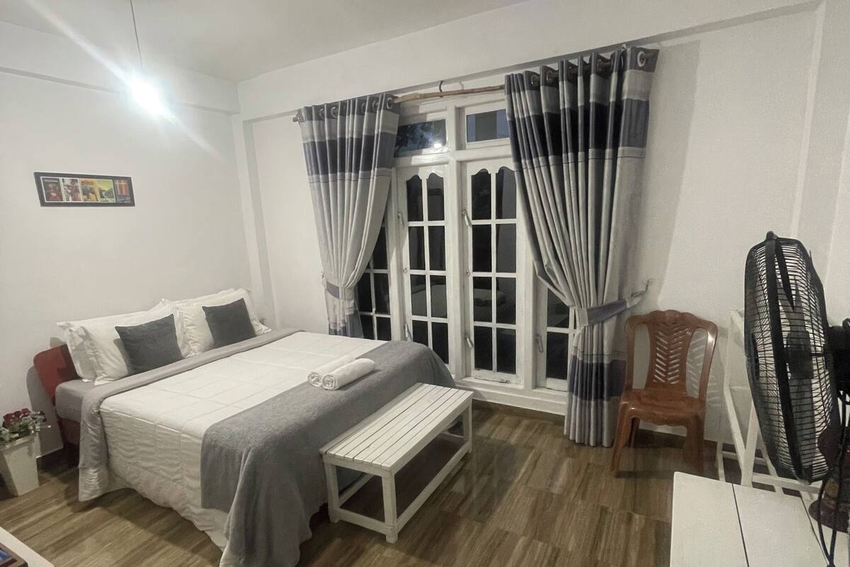 Ein Schlafzimmer mit Bett, Nachttisch, Stuhl und Schreibtisch mit Ventilator.