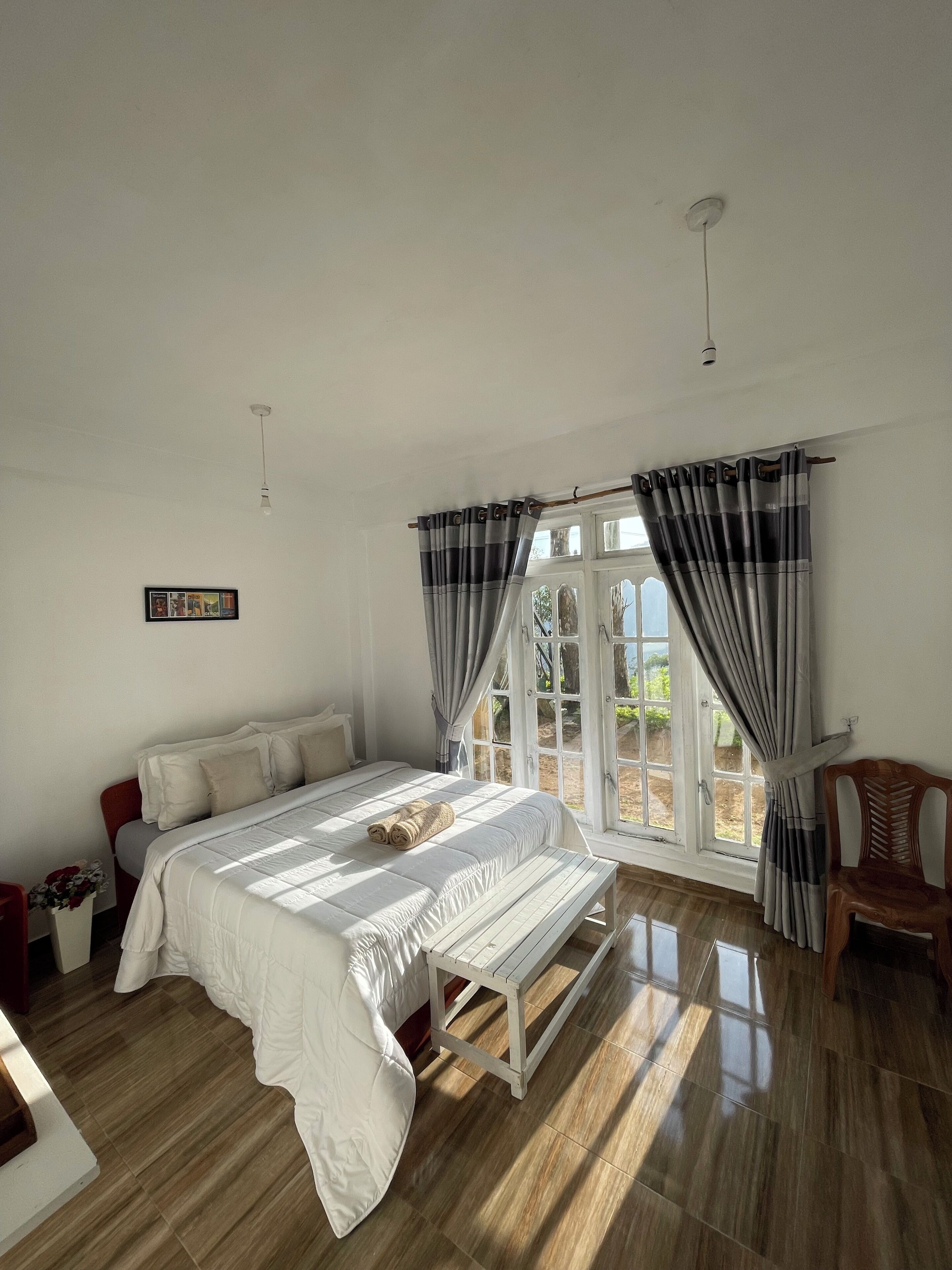 Une chambre à coucher avec un grand lit, un banc en bois, une chaise et une fenêtre avec des rideaux.
