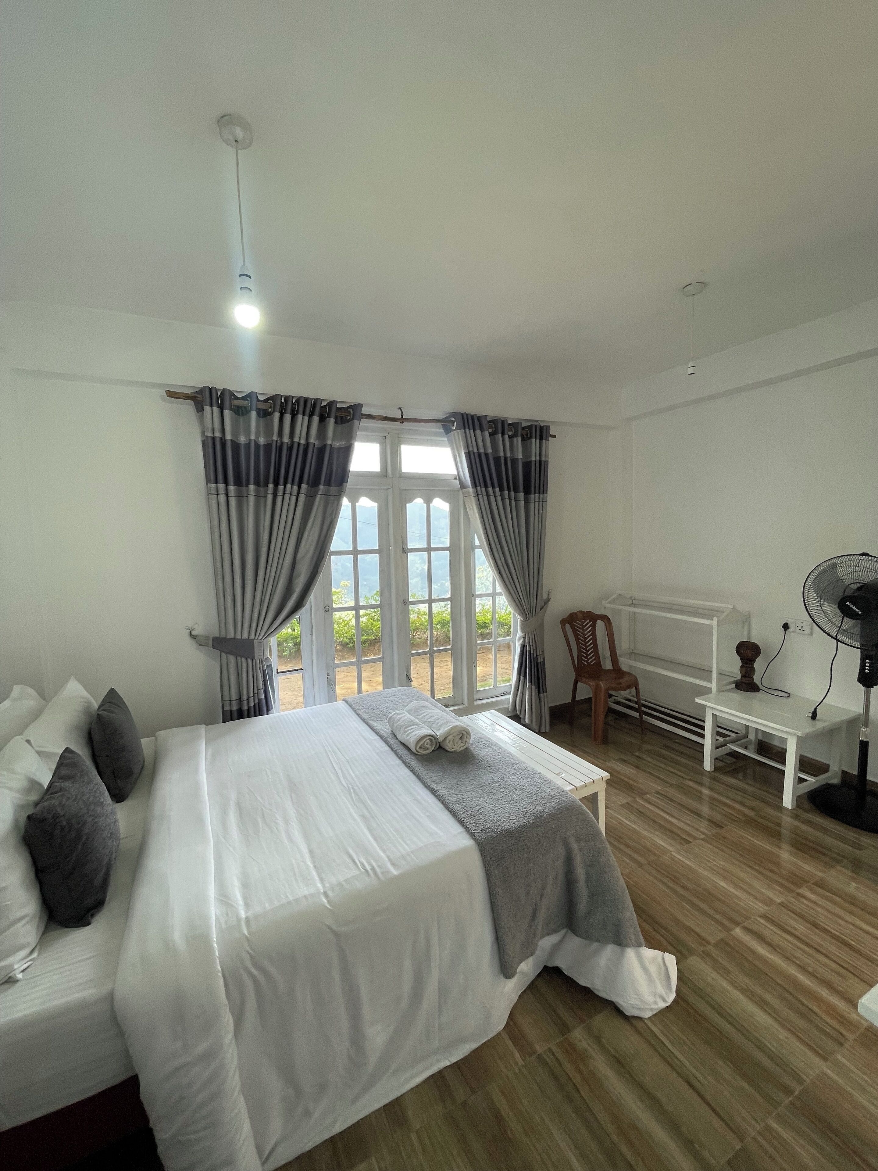 A bedroom with a large bed, a desk, a chair, and a window with curtains.