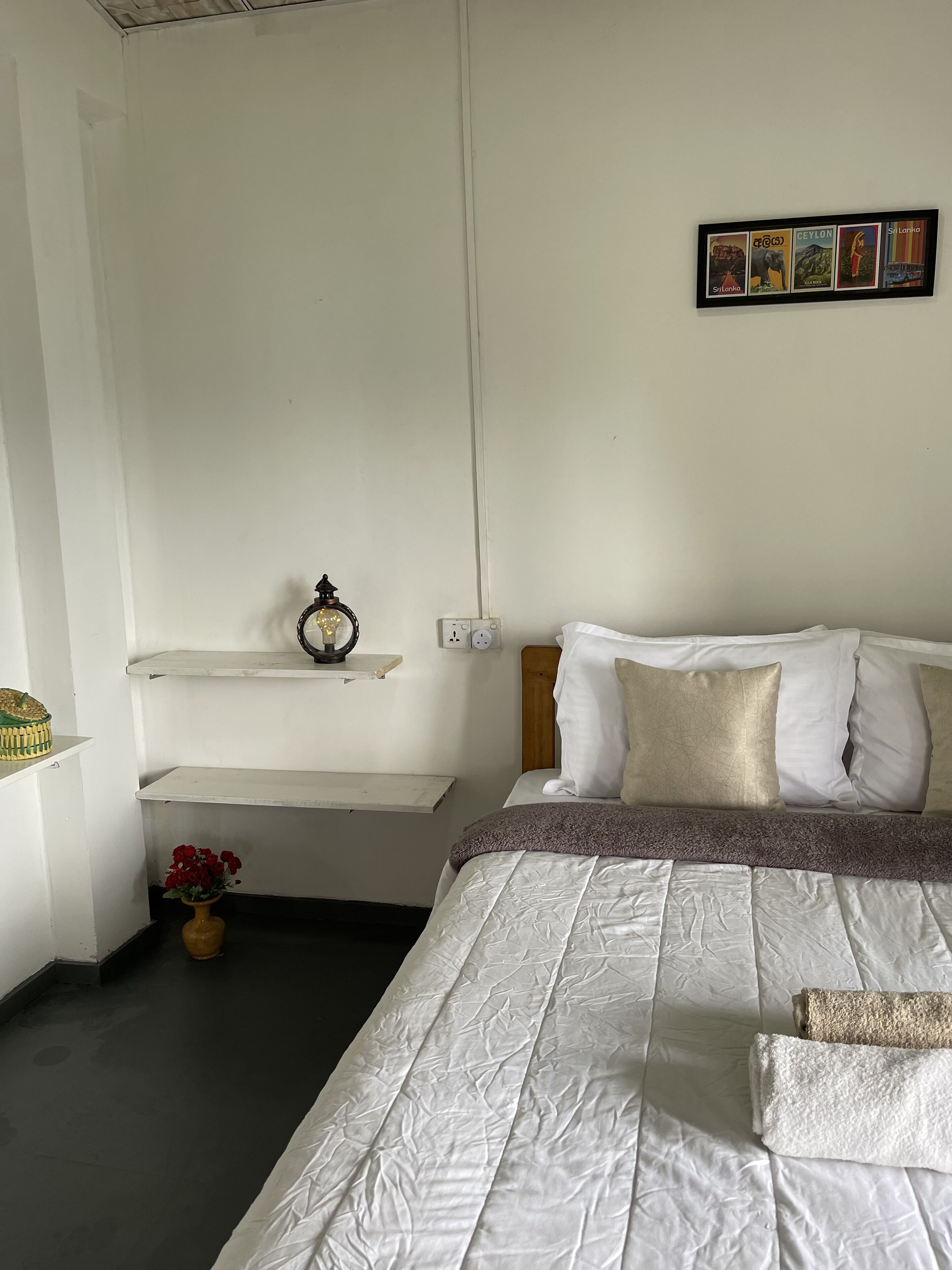 Un dormitorio ordenado con cama, almohadas, un estante con un objeto decorativo y un cuadro en la pared.