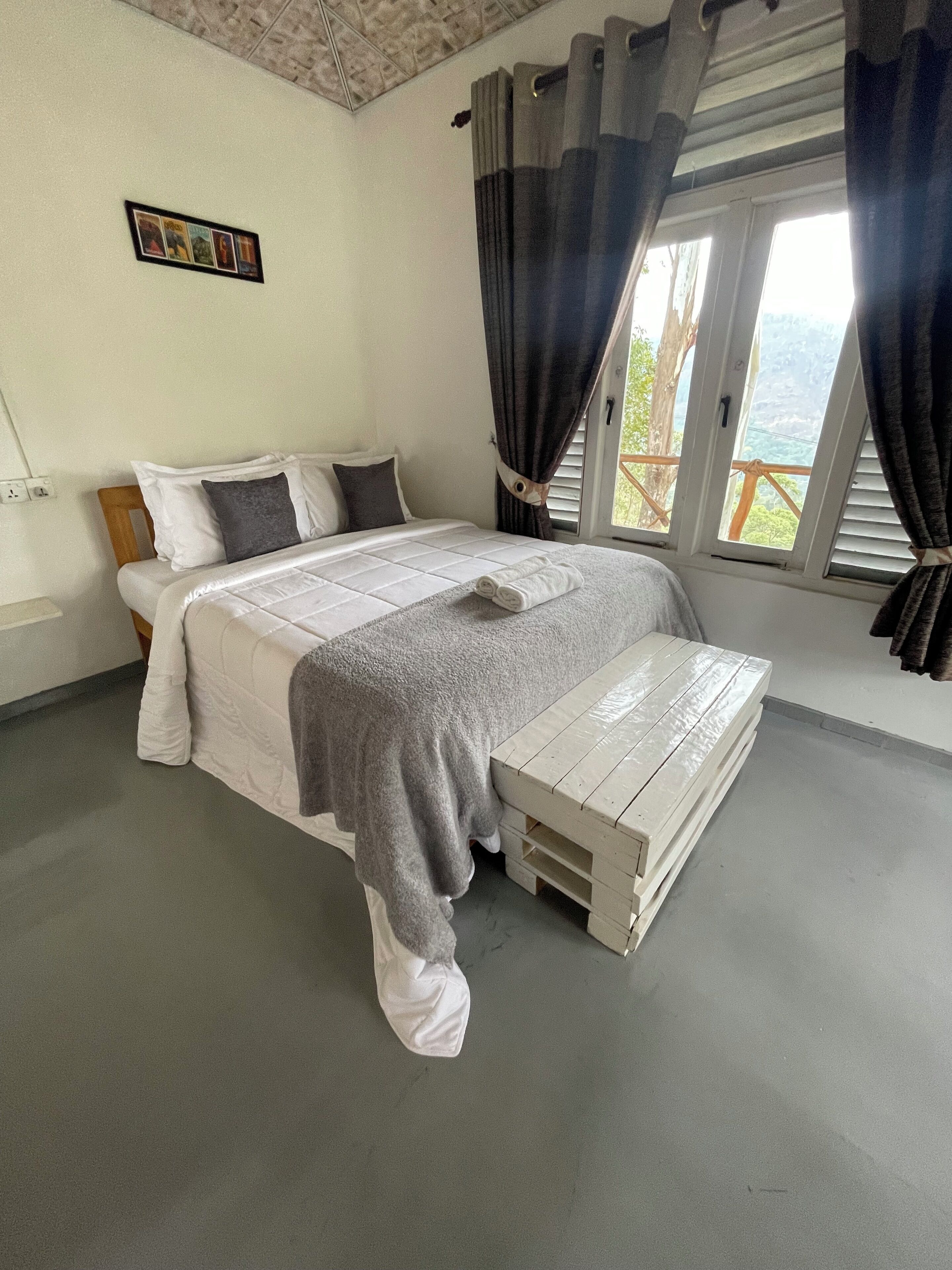 A neatly made bed with a grey blanket, white pillows, and a wooden headboard. There is a small picture frame on the wall above the bed.