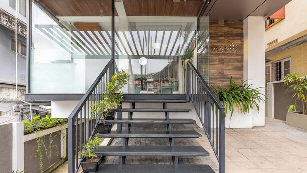 A modern staircase with glass railings and a wooden ceiling, leading to an indoor area with plants and a sign. - Treebo De Cloud 9 Regency (Thiruvananthapuram)