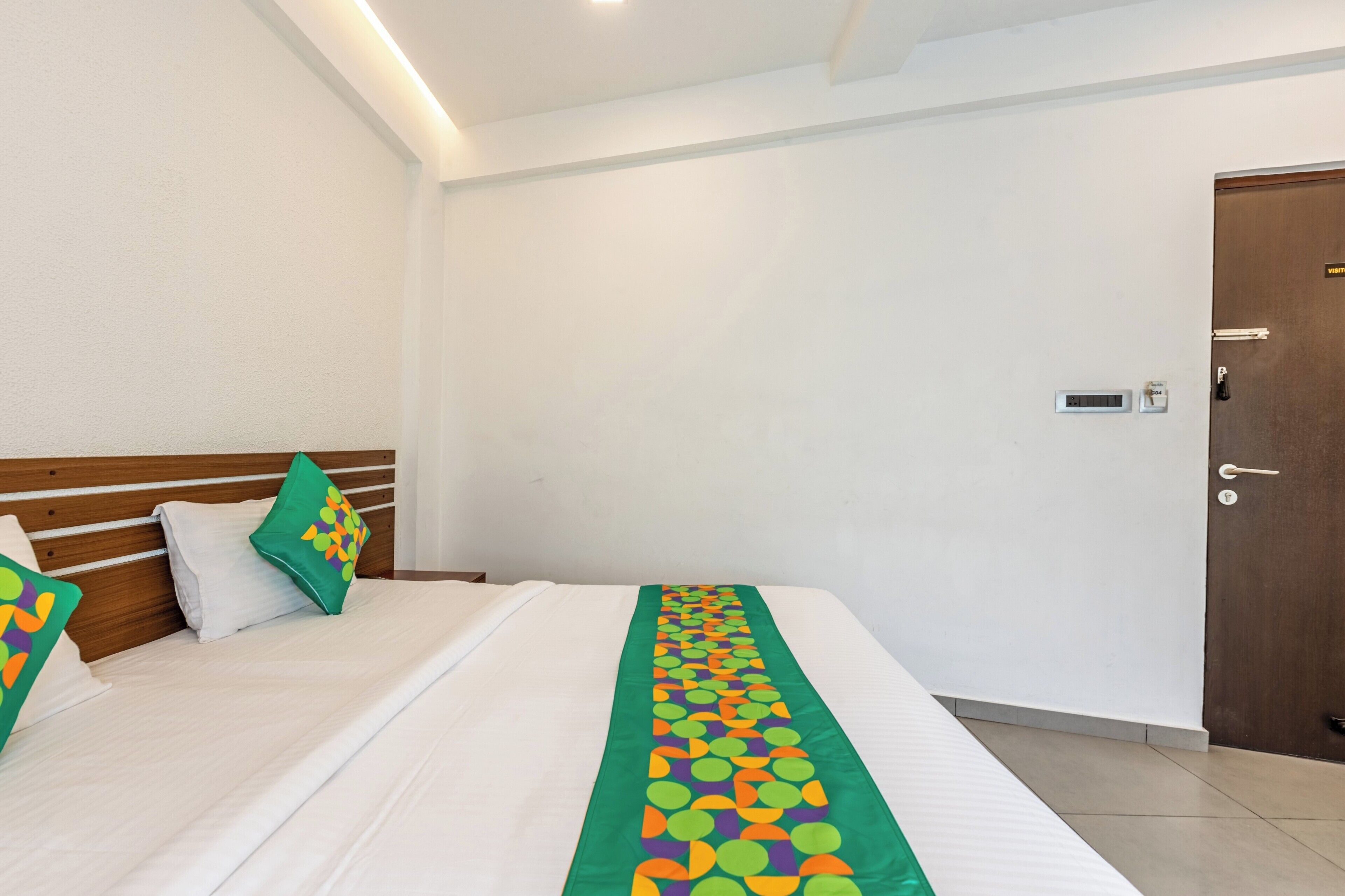 A hotel room with a neatly made bed, a wooden headboard, and a green and orange decorative runner.