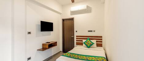 Un dormitorio con cama, ventilador de techo, televisor montado, estante de madera y una puerta.
