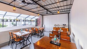 A modern dining area with wooden tables and chairs, overhead lighting, and a view of the city through large windows. - Treebo De Cloud 9 Regency (Thiruvananthapuram)