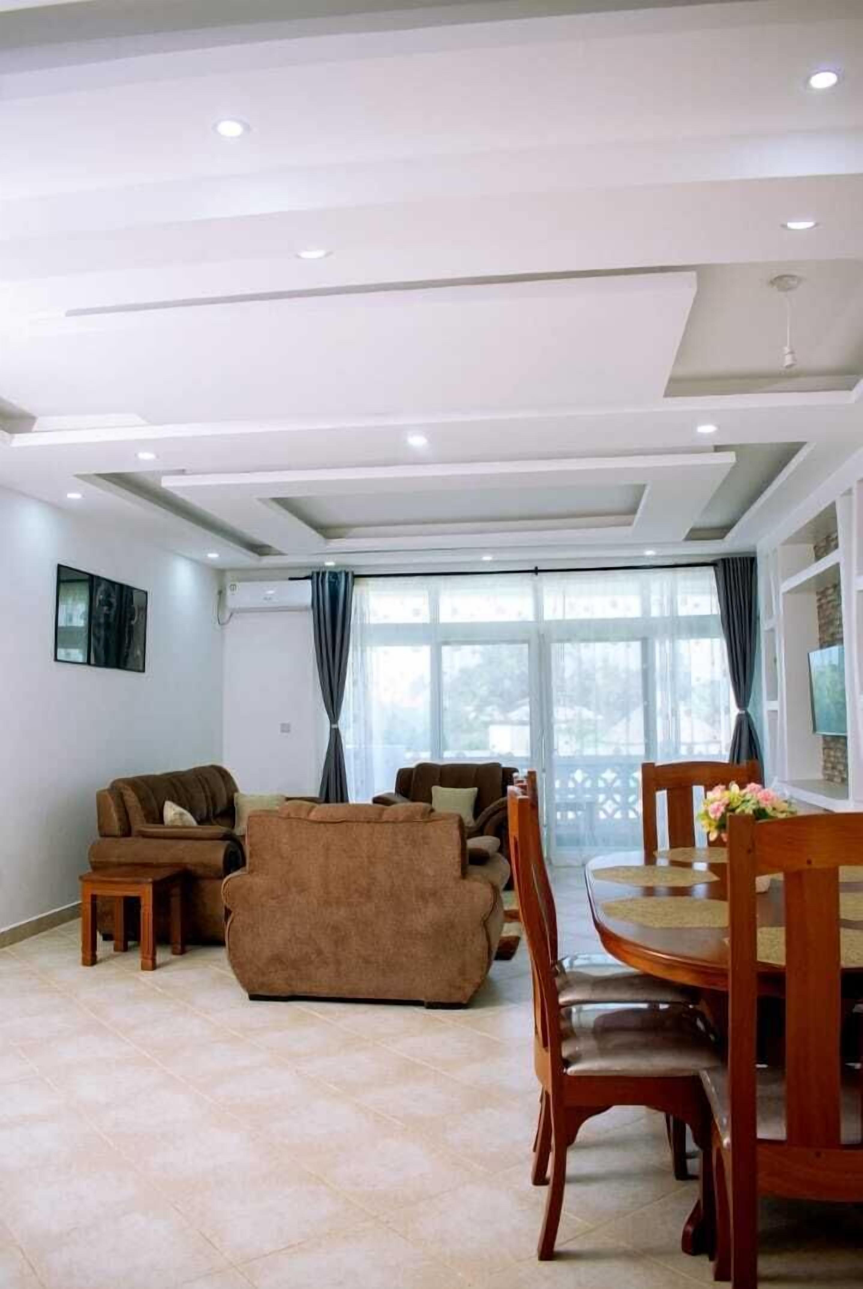 Un amplio salón con un conjunto de sofás, una mesa de comedor con sillas y un gran ventanal con cortinas.