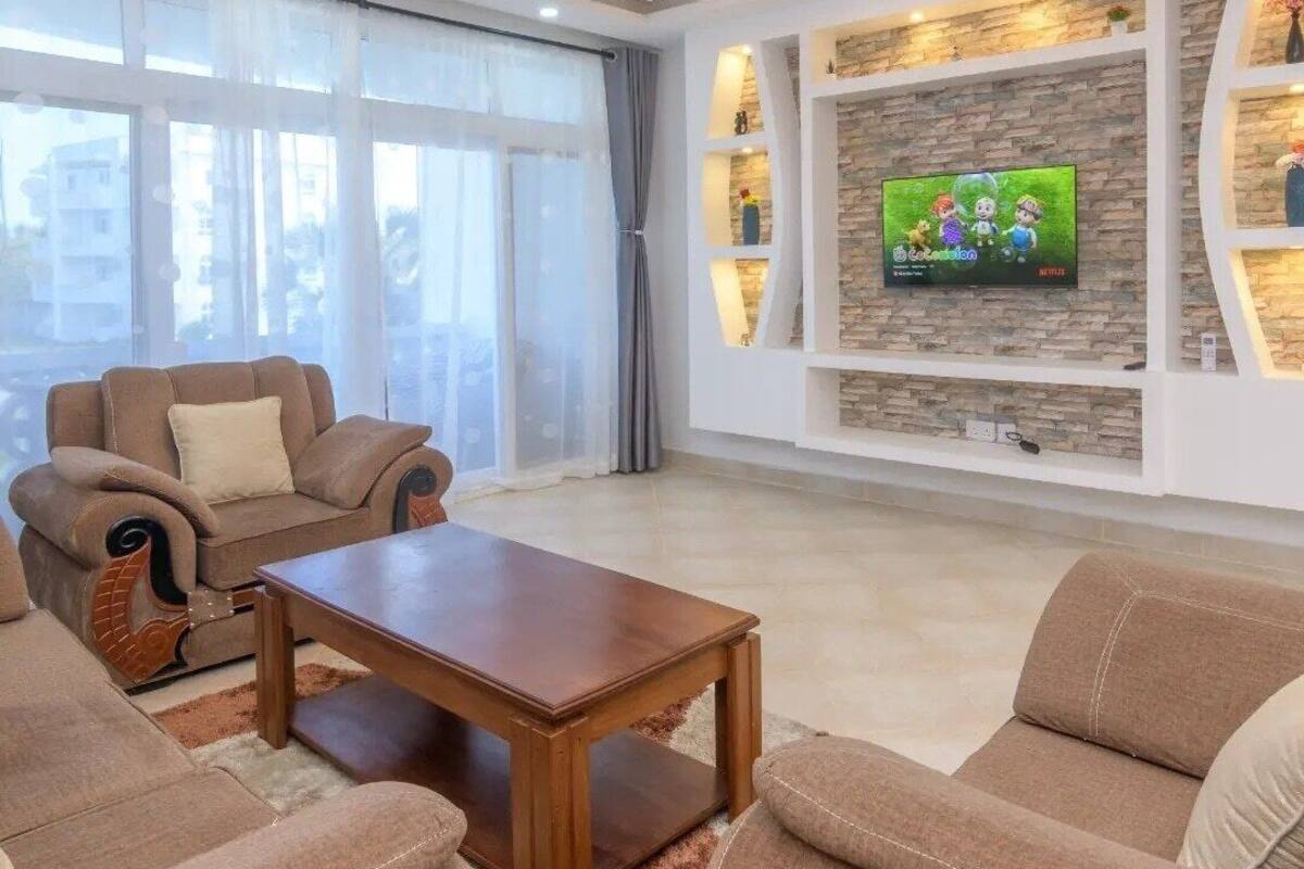 Un salon moderne avec un ensemble de canapés, une table basse et un téléviseur fixé au mur, qui est en pierre.