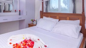 A bedroom with a four-poster bed, a bedside table with toiletries, a large window with curtains, and a mirror above the bed.