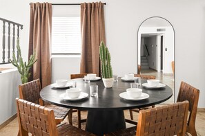 A round dining table with white plates and cups, surrounded by wooden chairs, with two potted cacti and brown curtains on a balcony. - Rock Climbing Wall~Pool& Mini Golf~Game Room~Mural (Peoria)