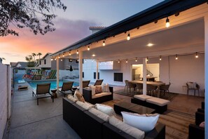 Un'area patio esterna con posti a sedere, una piscina e luci a catena.