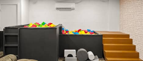 Ein Zimmer mit Spielbereich, einer Treppe und einer weißen Ziegelwand.